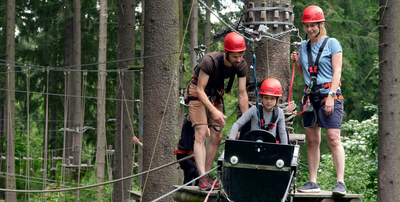 Ein Mann und eine Frau leisten einem Kind Hilfestellung an einer Seilbahn